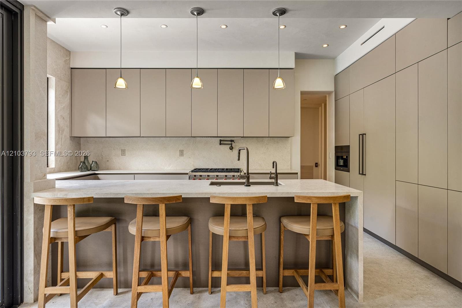 Minimalist kitchen featuring matte finish cabinetry, waterfall-edge stone countertop, built-in wall oven, three-light pendant fixture, and wall-mounted pot filler