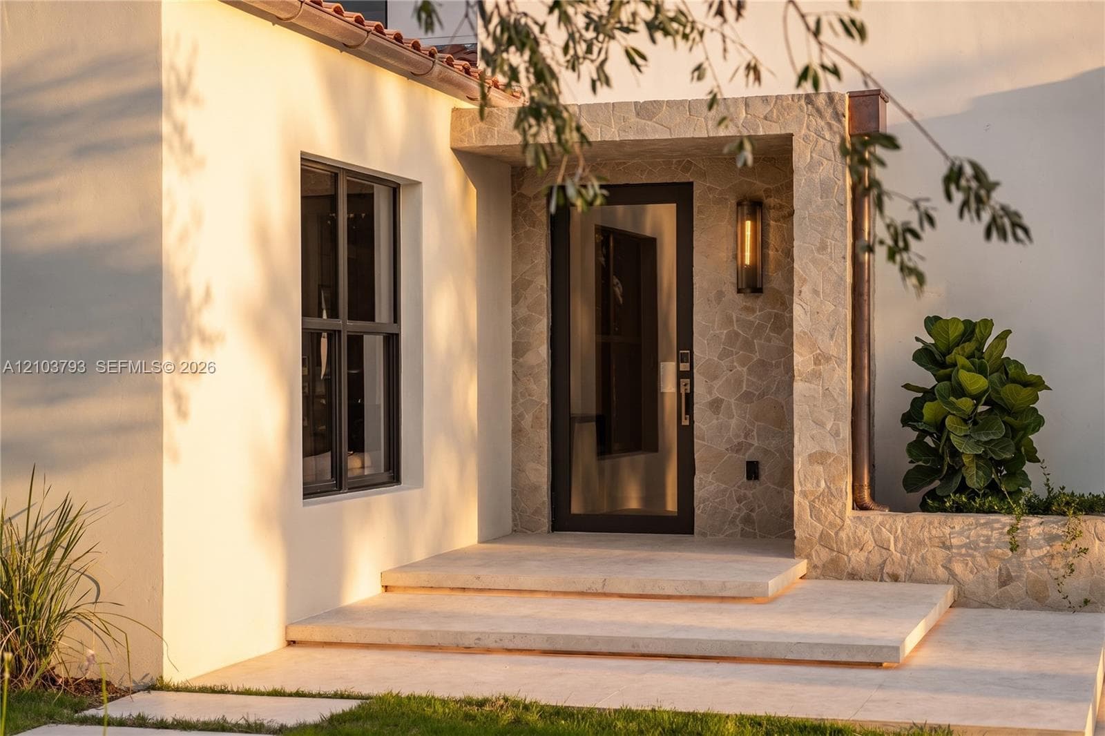 Entryway featuring neutral stone flooring, a full-length glass door with black frame, a contemporary multi-arm chandelier, and large windows with dark trim