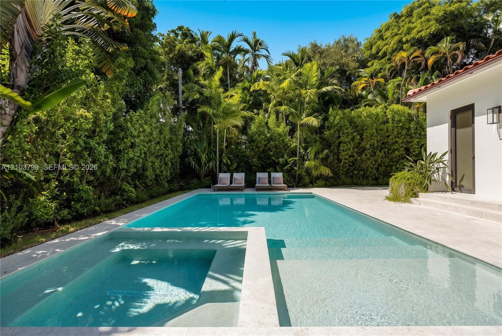 In-ground swimming pool with an integrated spa, stone-finish pool deck, and perimeter privacy landscaping