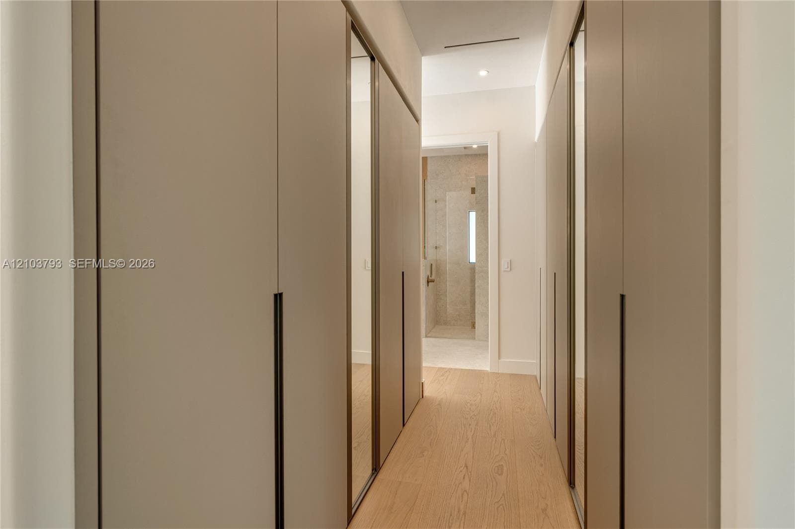 Floating vanity with dual rectangular undermount sinks, wood-finish wall paneling, frameless wall mirrors, metallic wall-mounted sconces, and stone tile shower surround