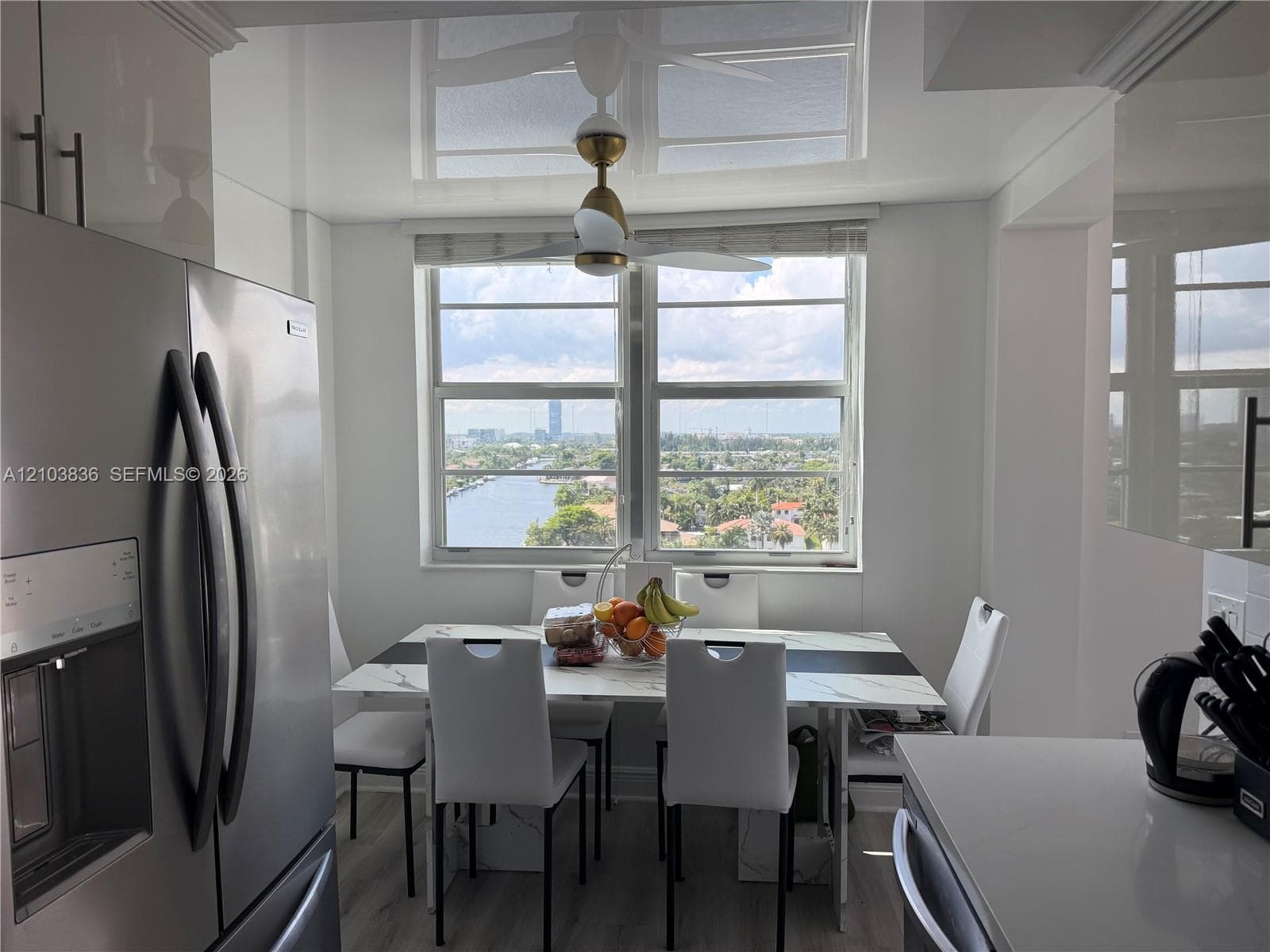 Stainless steel refrigerator, white cabinetry with dark pulls, wood-finish flooring, and a white dining table with seating