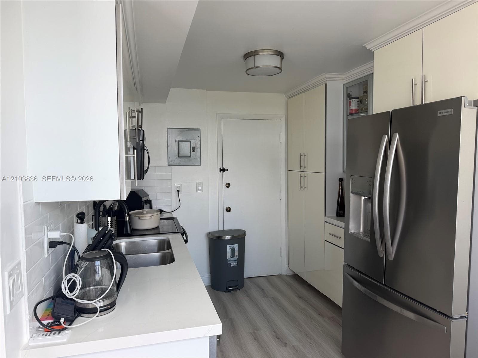 Galley kitchen with stainless steel appliances, white subway tile backsplash, light wood-finish flooring, and ample cabinetry