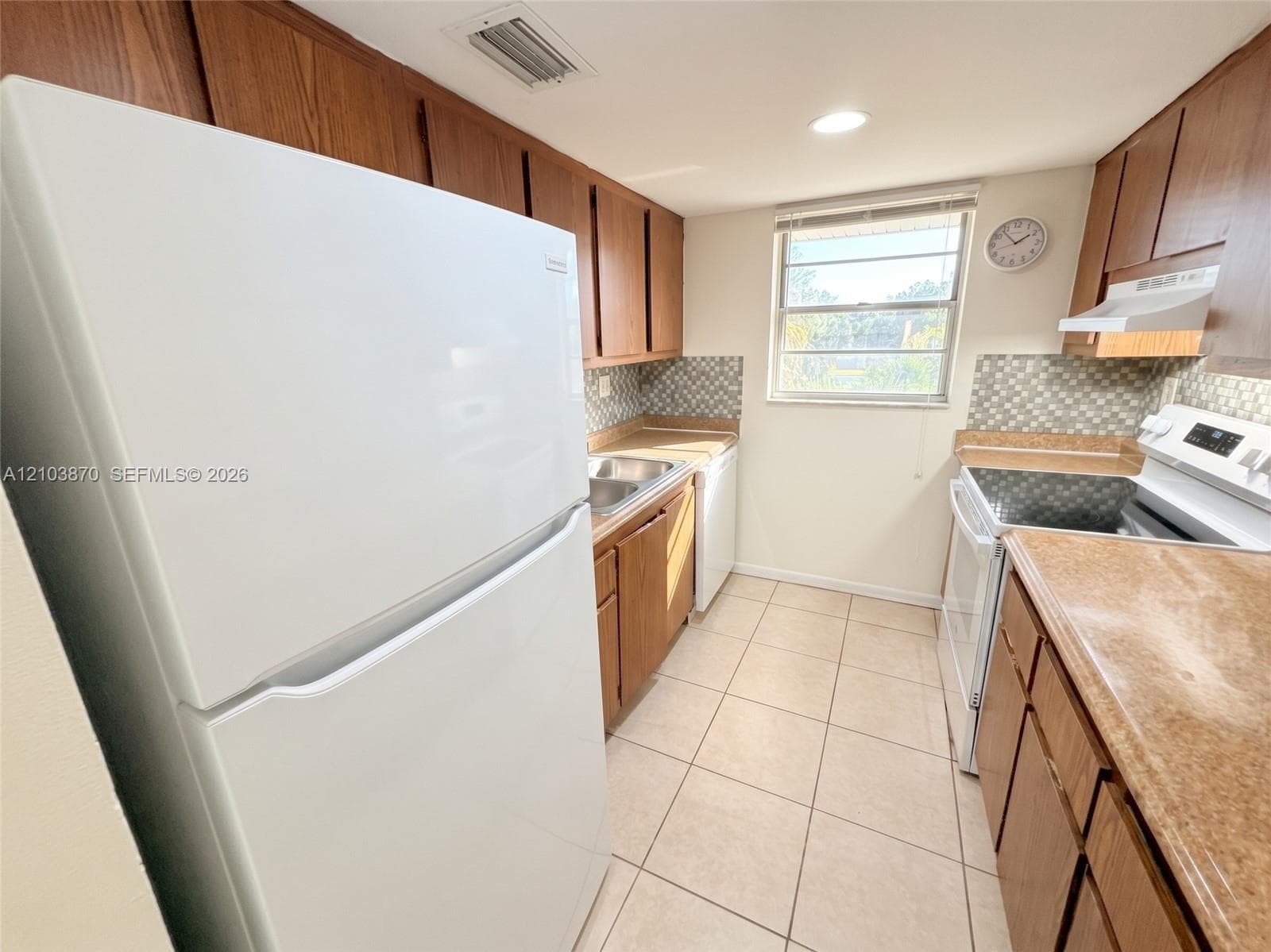 Kitchen featuring wood cabinetry, solid-surface countertops, mosaic tile backsplash, ceramic tile flooring, and white kitchen appliances