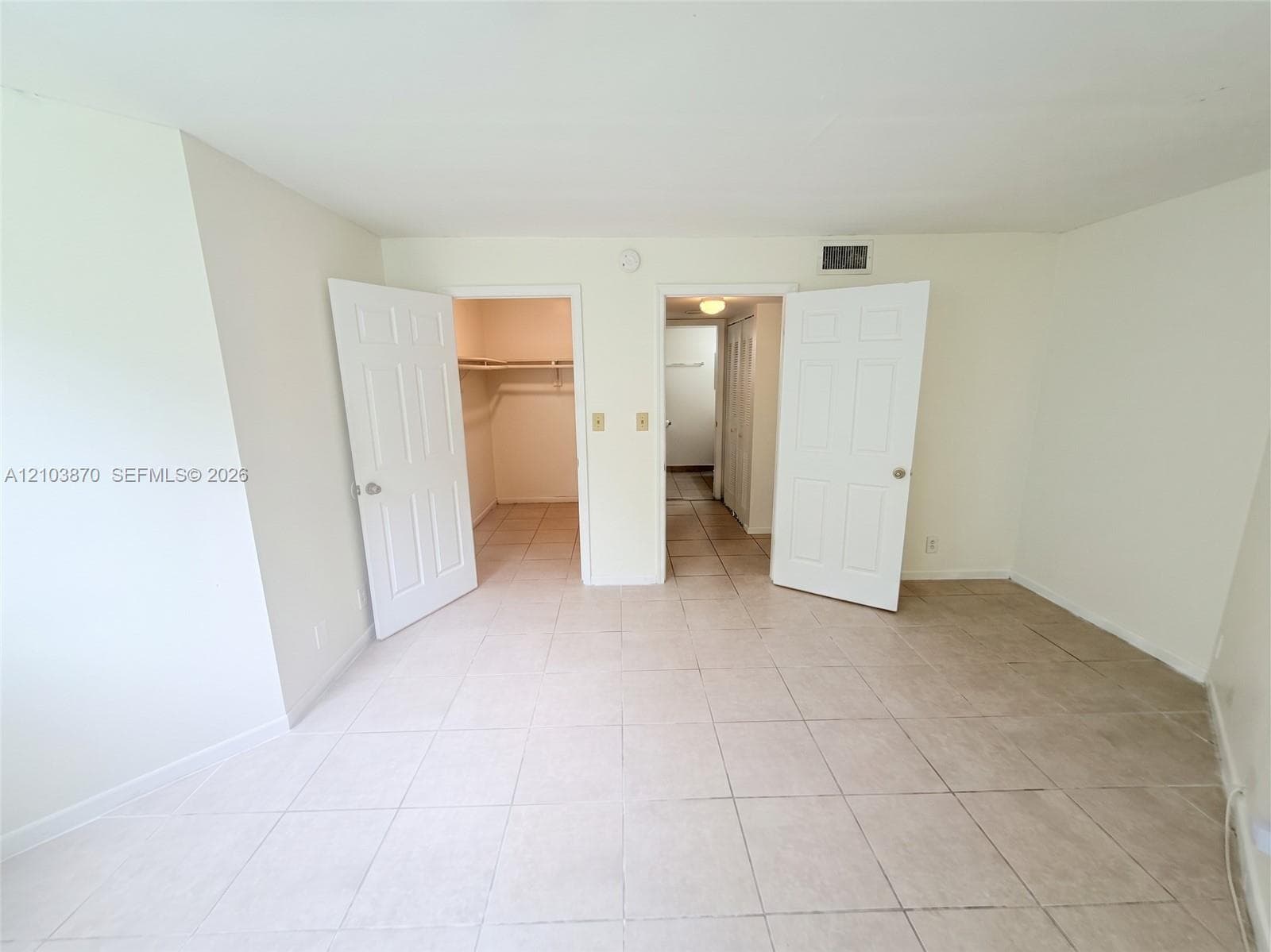 Neutral-toned ceramic tile flooring, two six-panel interior doors, and built-in closet shelving