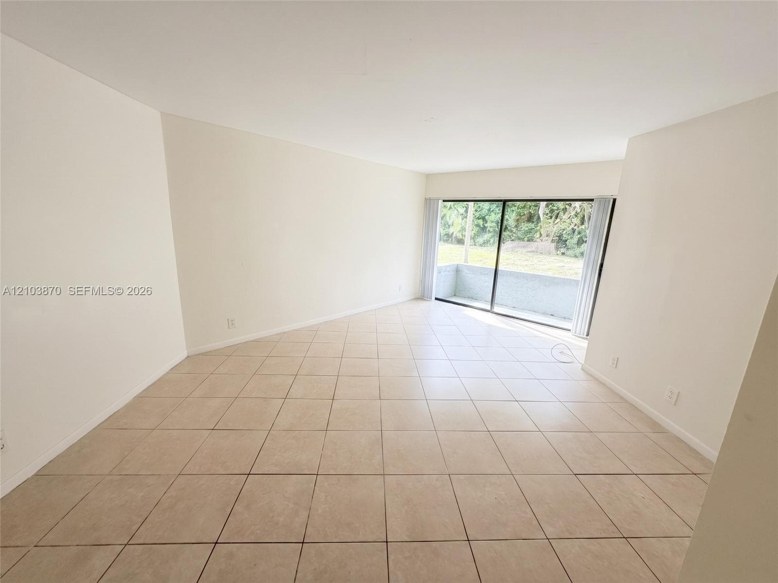 Spacious room featuring neutral ceramic tile flooring and floor-to-ceiling sliding glass doors opening to an exterior patio