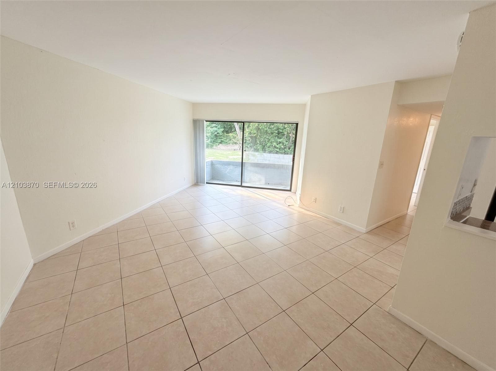 Open-concept area featuring light-toned tile flooring, neutral wall paint, and sliding glass doors with access to an exterior patio