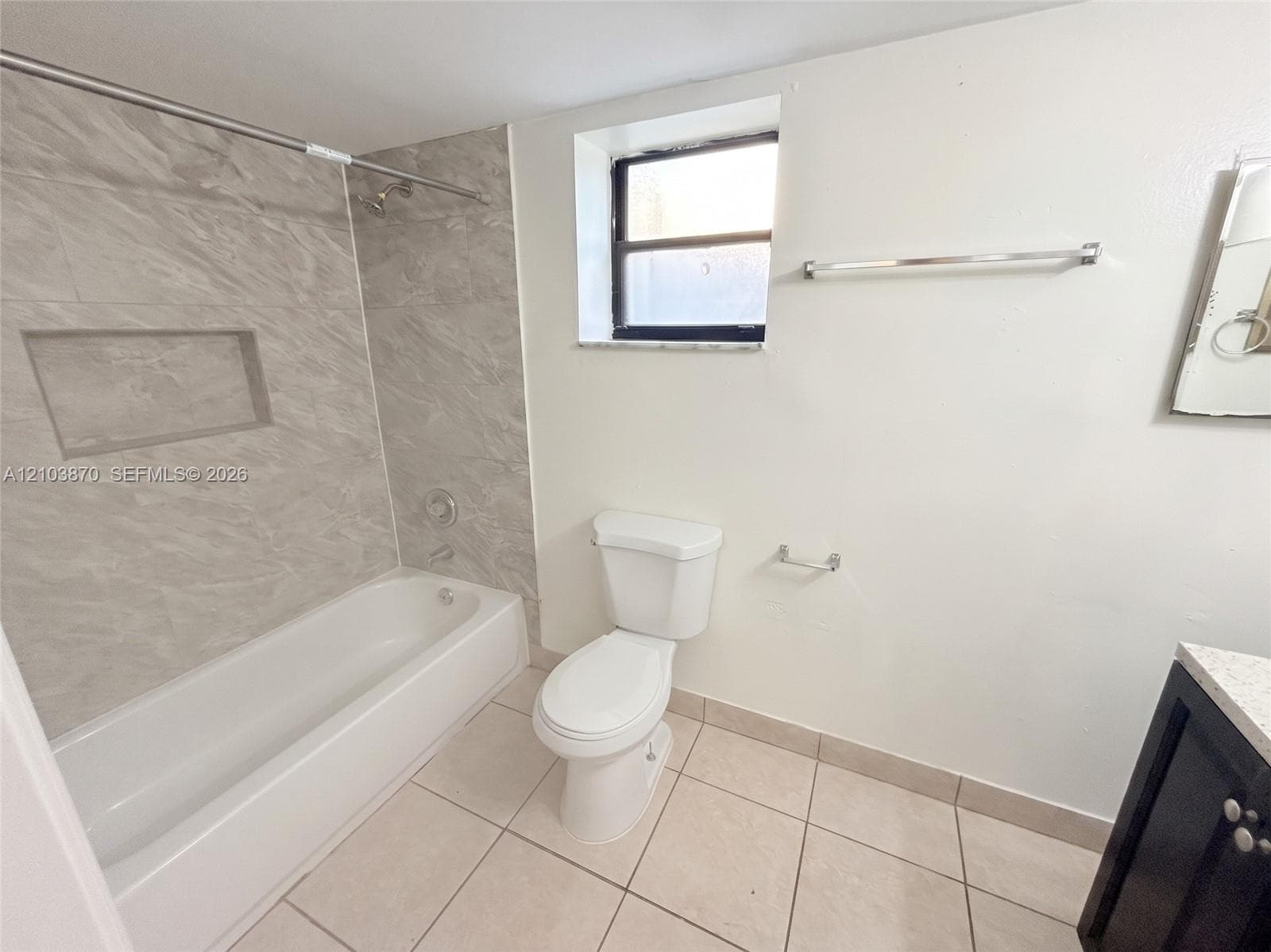 Bathroom featuring a soaking tub with stone-finish surround, recessed shower niche, ceramic tile flooring, and a vanity with a light-toned countertop