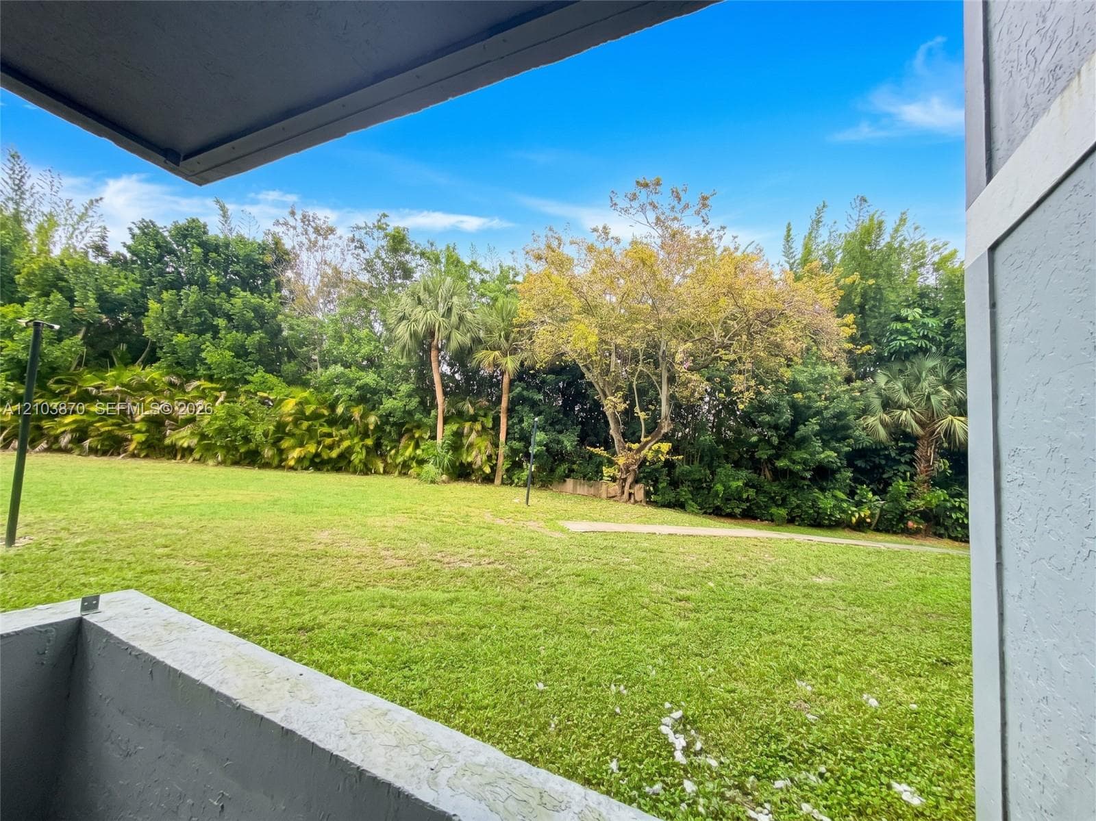 Covered concrete balcony overlooking an expansive lawn with mature trees and perimeter landscaping