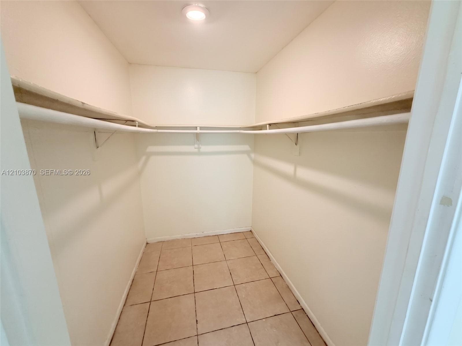 Storage area featuring tile flooring, ceiling-mounted lighting, and integrated shelving with garment rods