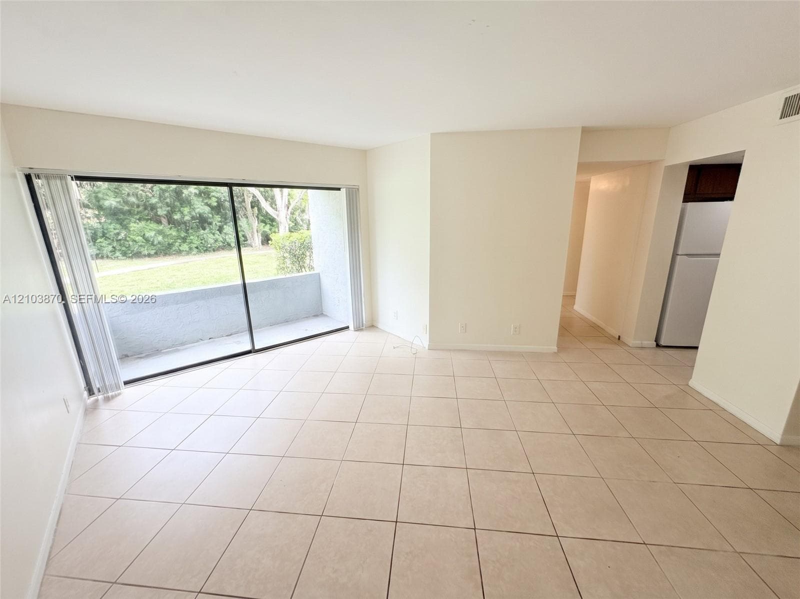 Spacious room featuring neutral ceramic tile flooring and floor-to-ceiling sliding glass doors opening to an exterior patio