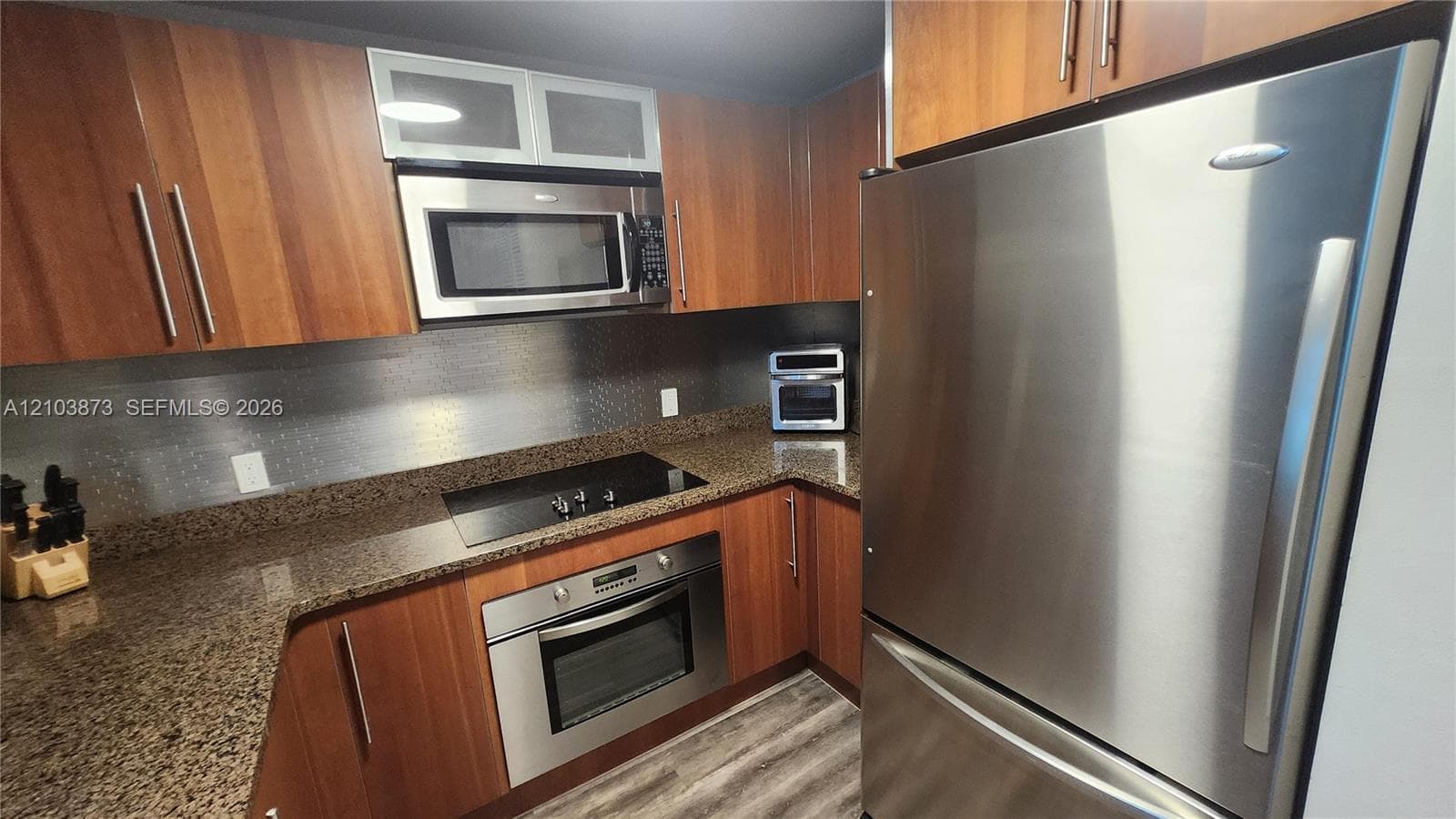 Kitchen featuring wood-finish cabinetry, stone countertops, stainless steel appliances, built-in microwave, and wood-finish flooring