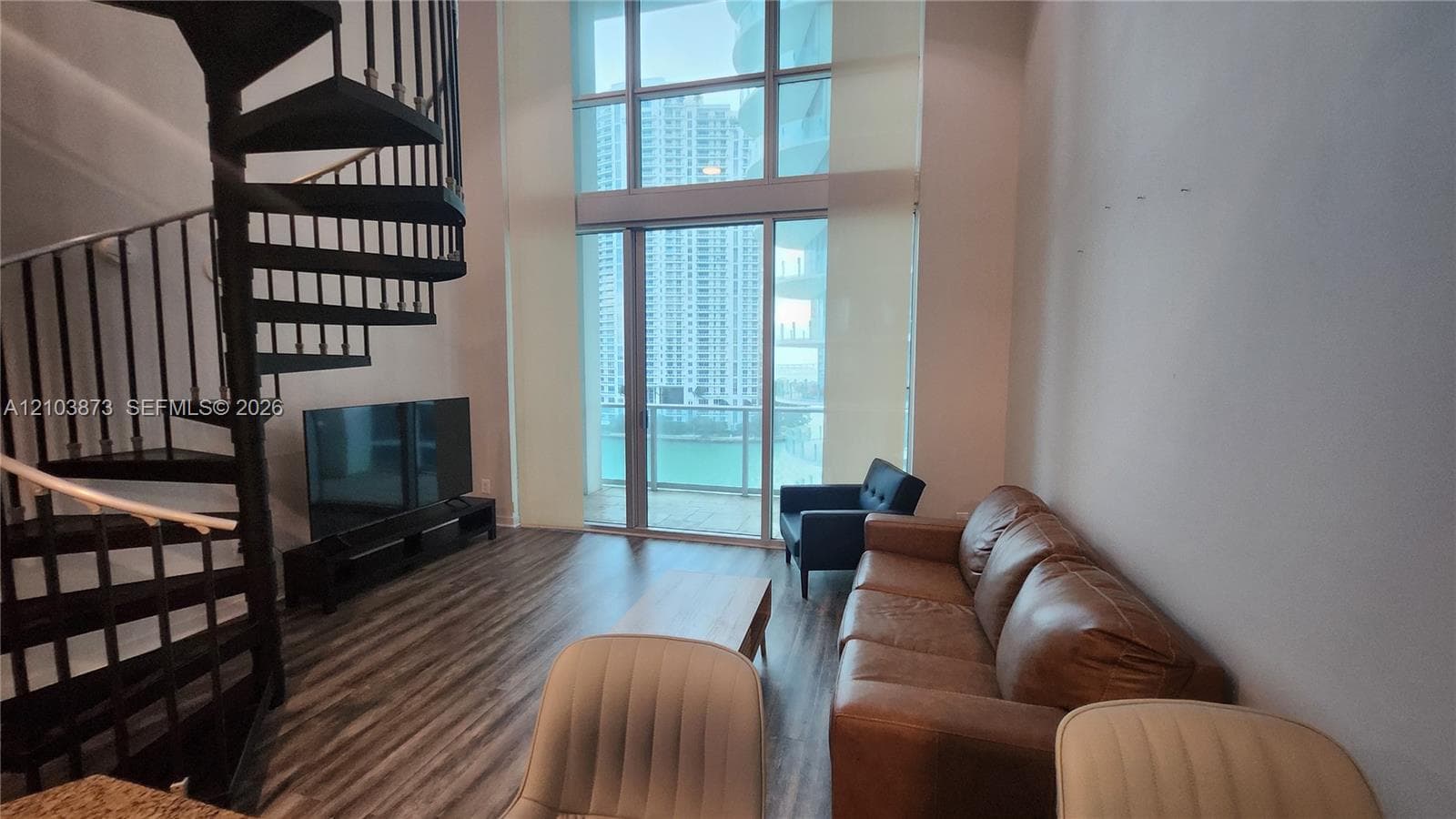 Double-height floor-to-ceiling windows, metal spiral staircase, and wood-finish flooring