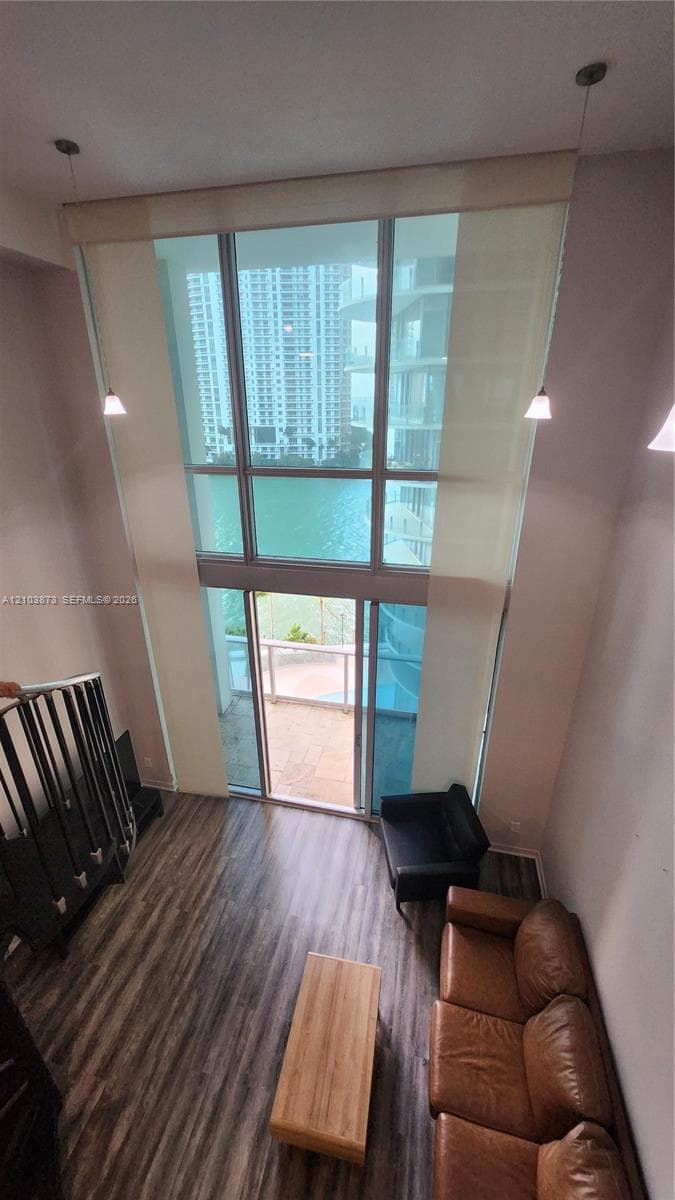 Double-height floor-to-ceiling windows, wood-finish flooring, metal staircase railing, and pendant lighting