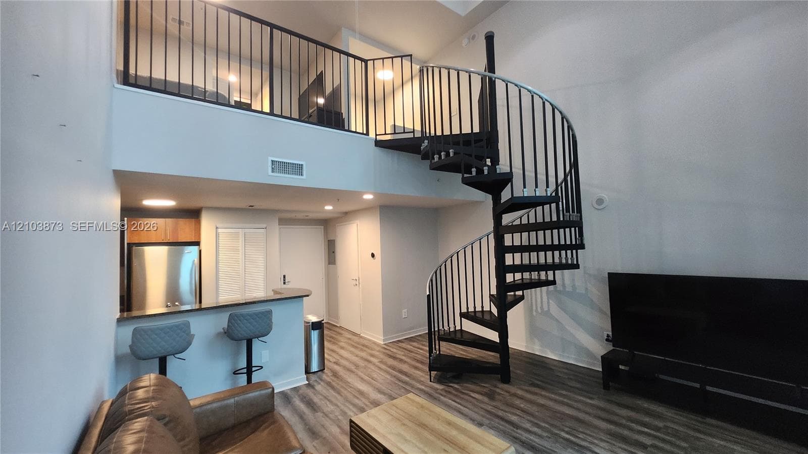 Spiral staircase with black metal railing, wood-finish flooring, built-in breakfast bar, and mezzanine level with matching iron railing
