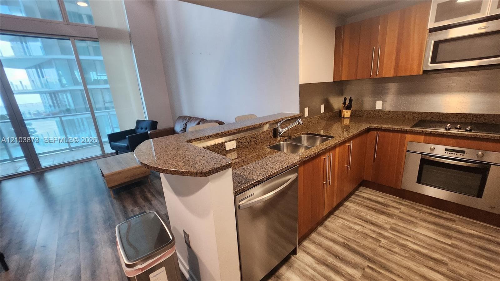Kitchen featuring wood-finish cabinetry, stone-surface countertops, stainless steel appliances, a dual-basin undermount sink, and wood-finish flooring