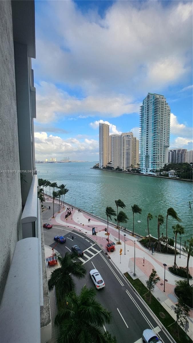 Exterior balcony featuring a concrete railing with unobstructed water, city skyline, and waterfront promenade surroundings