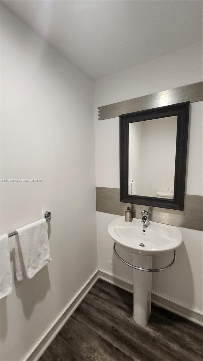Pedestal sink with integrated chrome towel ring, wall-mounted mirror with a dark frame, metallic decorative wall inlay, and wood-finish flooring
