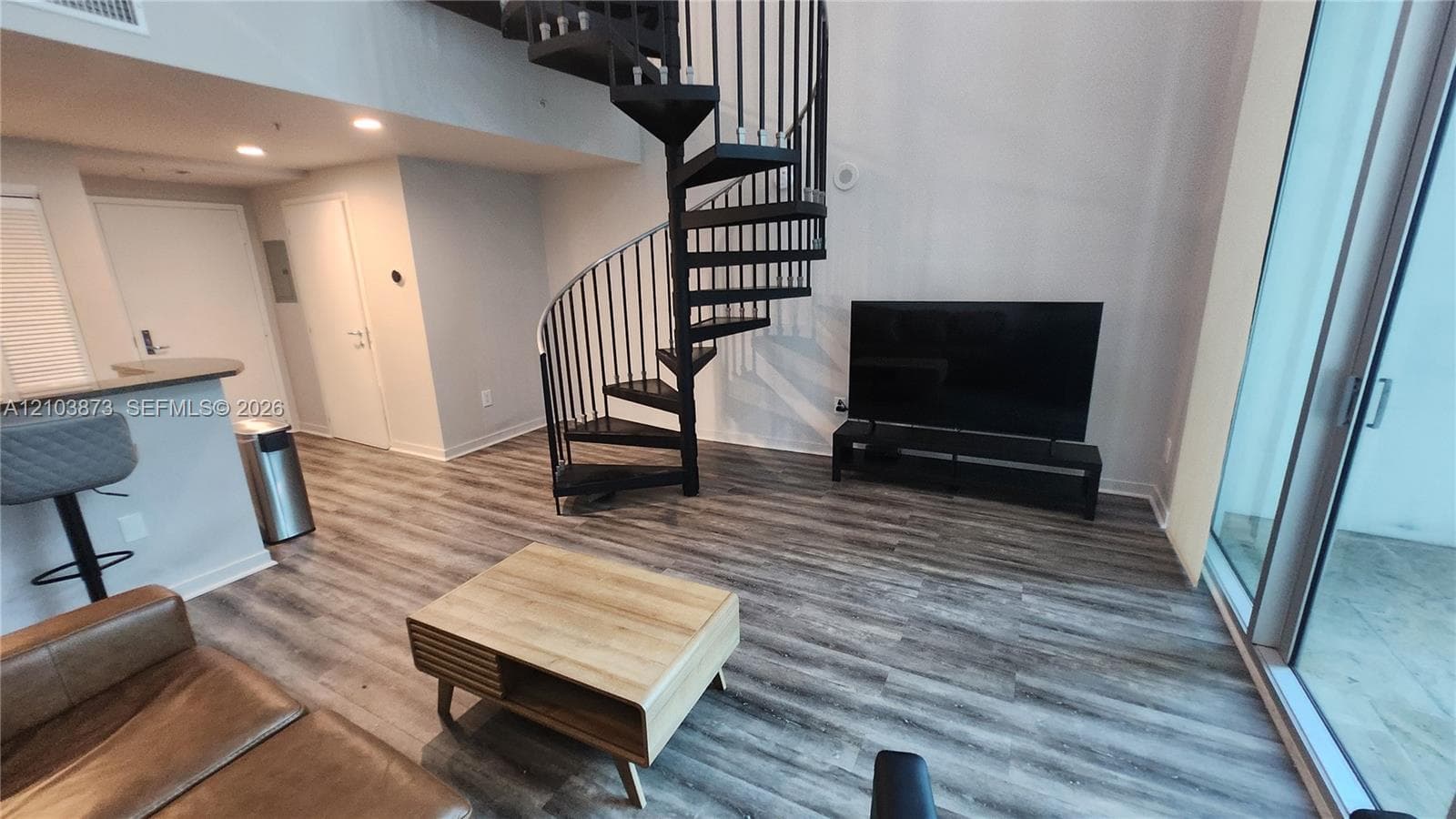 Open-concept interior featuring wood-finish flooring, a black metal spiral staircase, recessed lighting, and a floor-to-ceiling glass sliding door