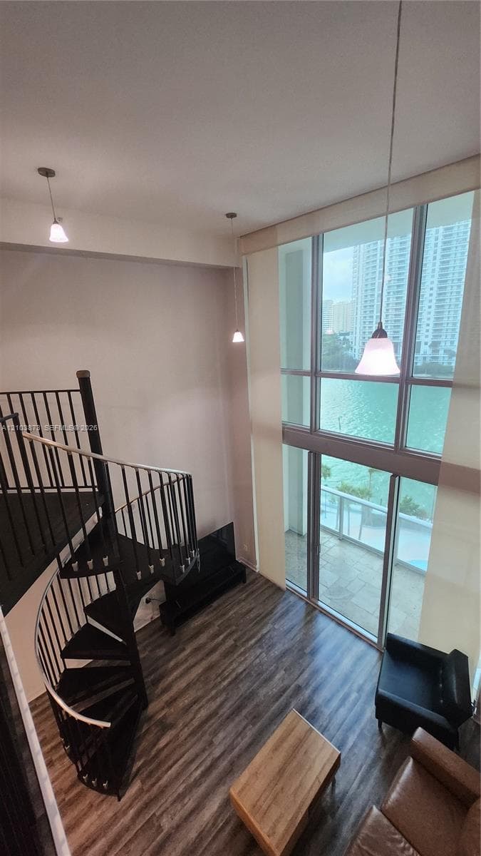 Double-height floor-to-ceiling windows, spiral staircase with metal railings, wood-finish flooring, and pendant lighting