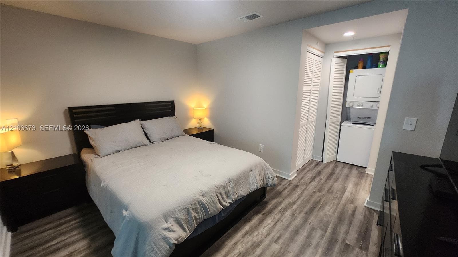 Wood-finish flooring, recessed ceiling lighting, and double-door louvered closet housing a built-in stackable washer and dryer unit