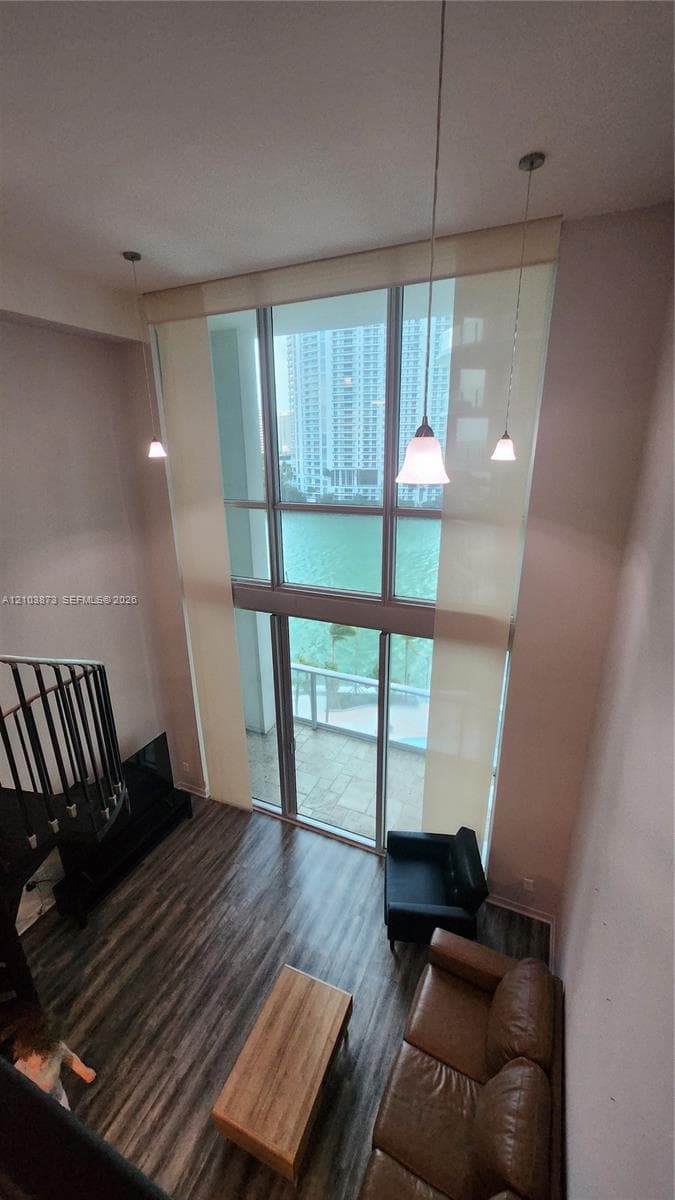 Double-height windows with floor-to-ceiling glass, wood-finish flooring, metal spiral staircase, and three pendant light fixtures