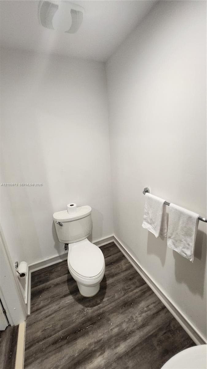 Powder room featuring wood-finish flooring, a white porcelain toilet, and a wall-mounted metal towel rack