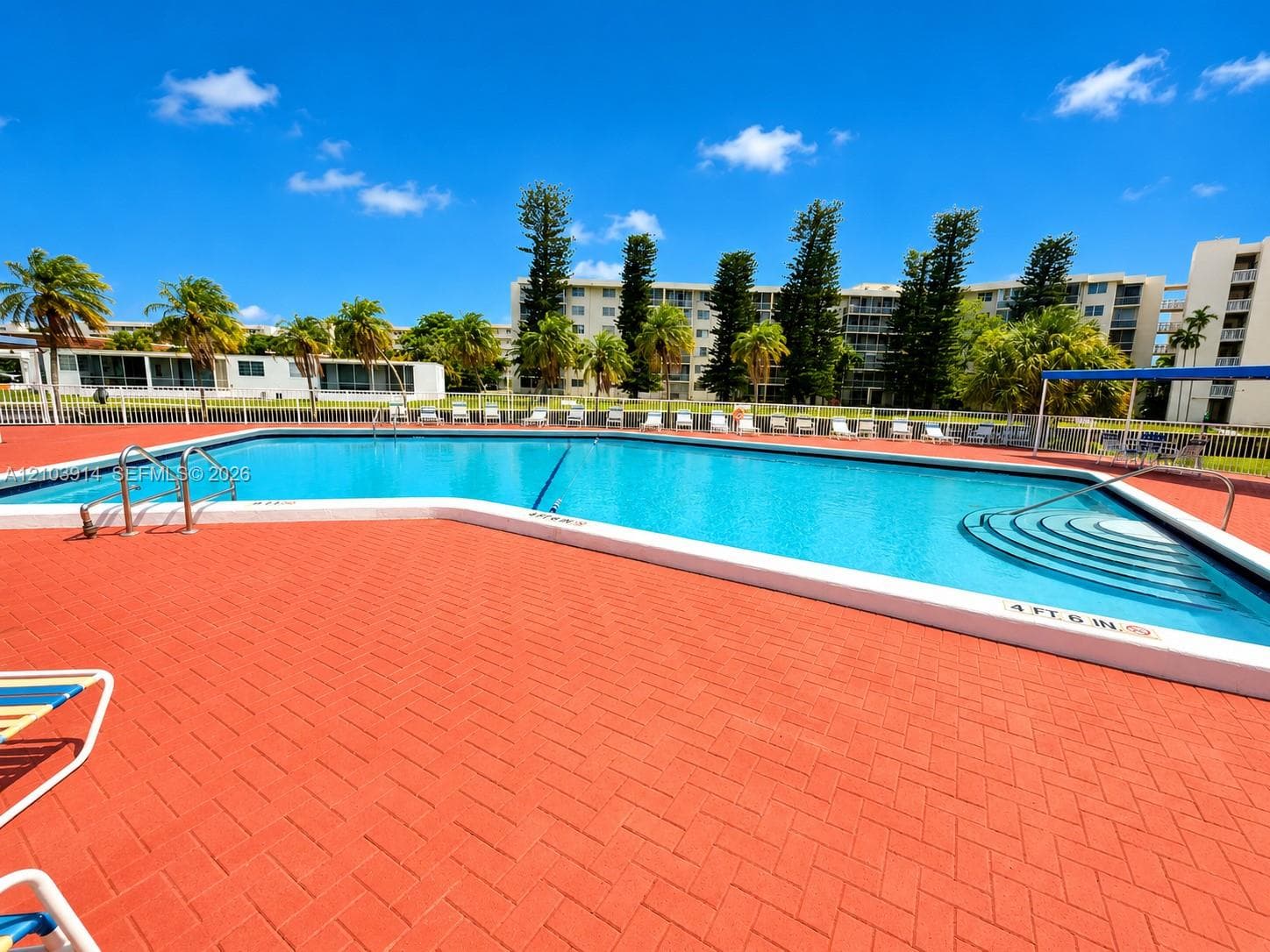 Swimming pool featuring a herringbone-patterned paved deck, integrated stairs for entry, stainless steel handrails, and surrounding perimeter fencing
