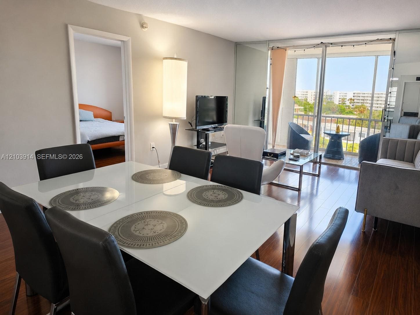 Living area featuring wood-finish flooring, floor-to-ceiling mirrored walls, and sliding glass doors with access to an exterior balcony