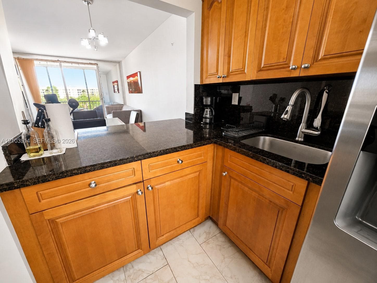 Kitchen featuring wood cabinetry, stone countertops, stainless steel undermount sink with pull-down faucet, and tiled flooring