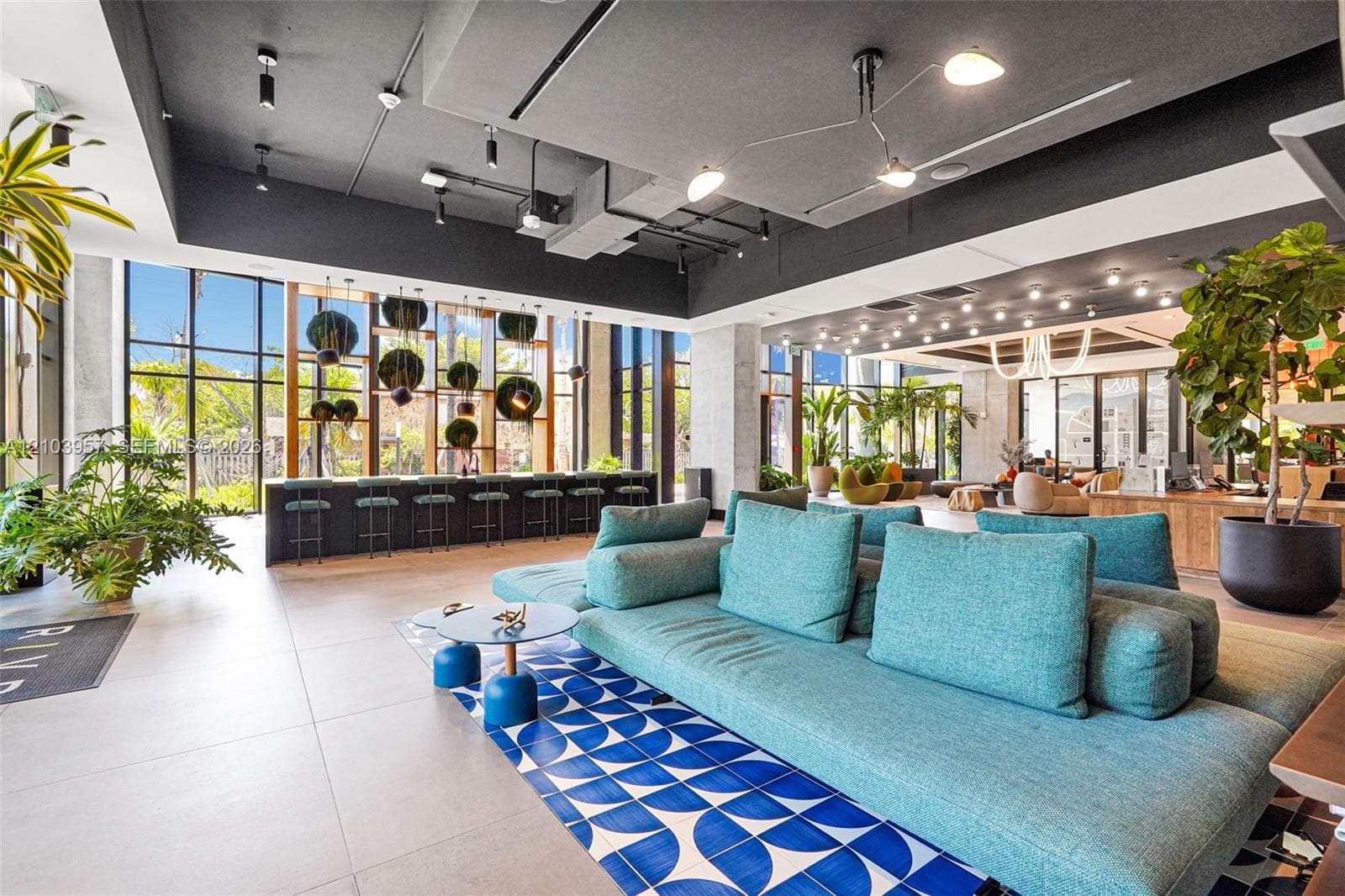 Expansive lounge area featuring floor-to-ceiling windows, a long bar area with seating, recessed lighting, and a patterned tile accent rug