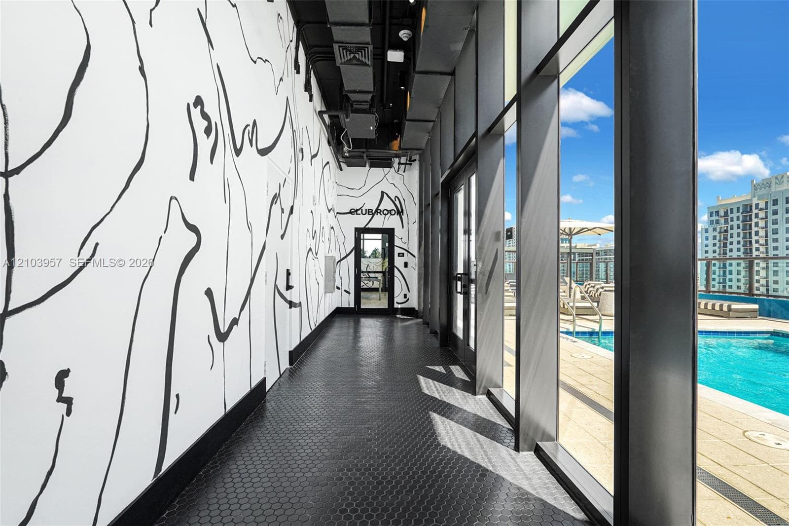 Hallway featuring patterned wall treatment, hexagonal tile flooring, and floor-to-ceiling windows overlooking an outdoor pool and distant buildings