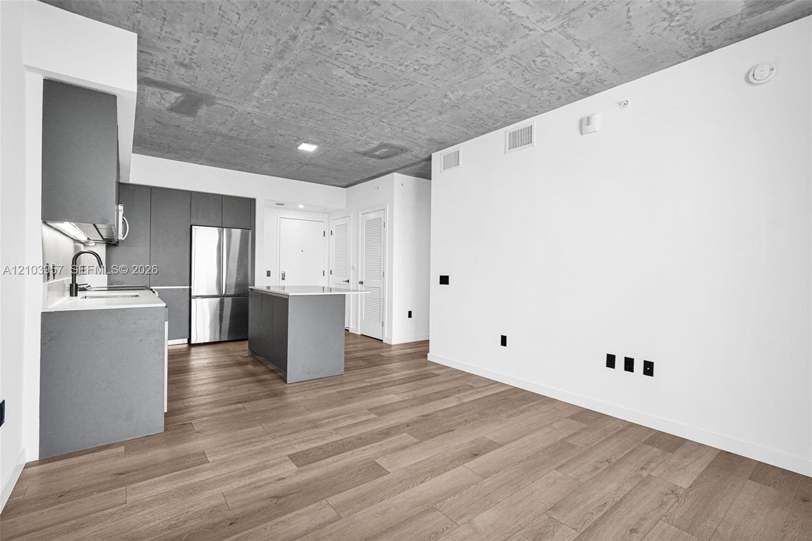 Open-concept living area featuring wood-finish flooring, a textured concrete ceiling, and a modern kitchen with flat-panel cabinetry, a stainless steel refrigerator, and a kitchen island