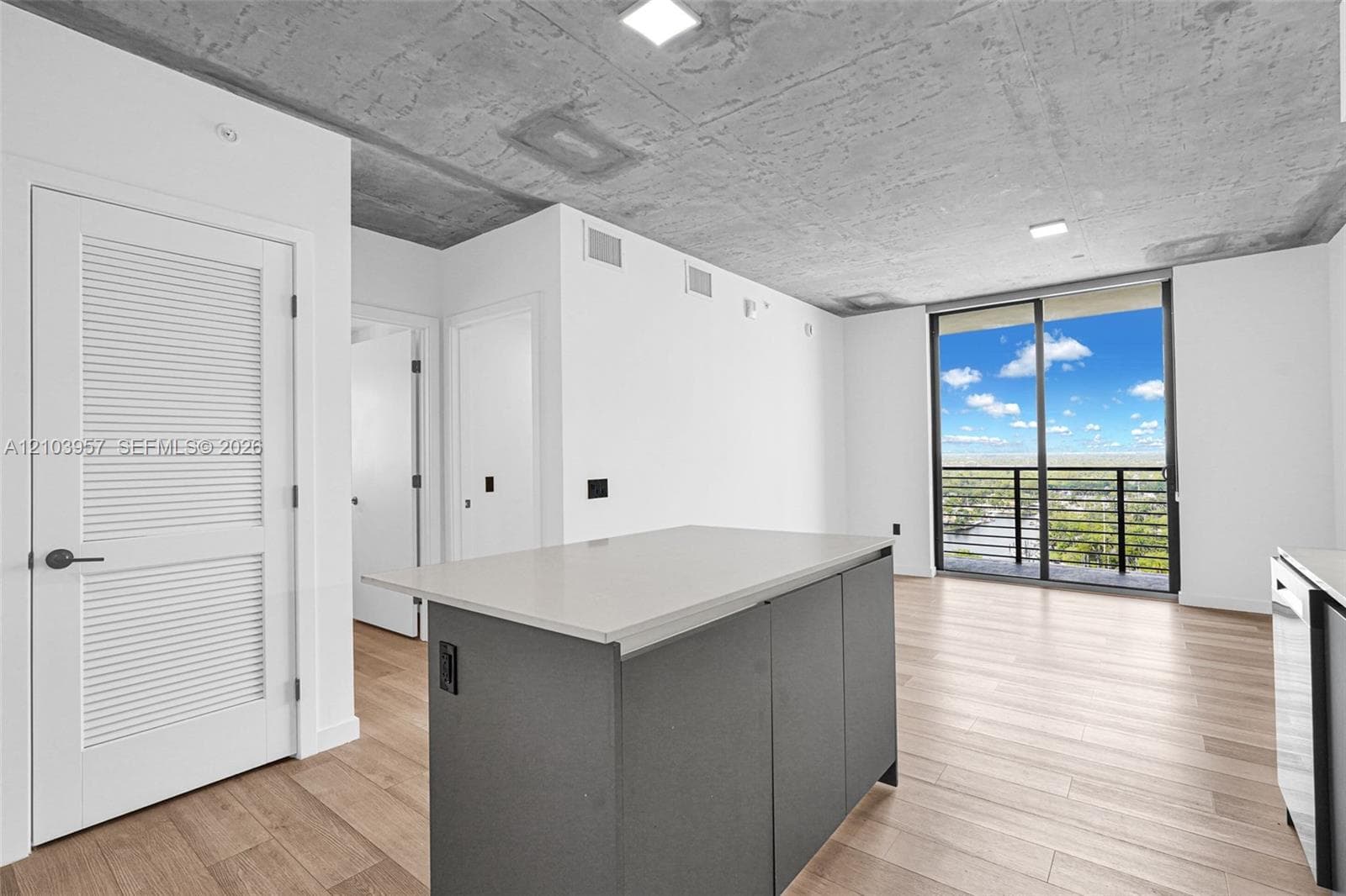 Expansive sliding glass doors, concrete ceiling, wood-finish flooring, central island with light-toned countertop, and modern appliances