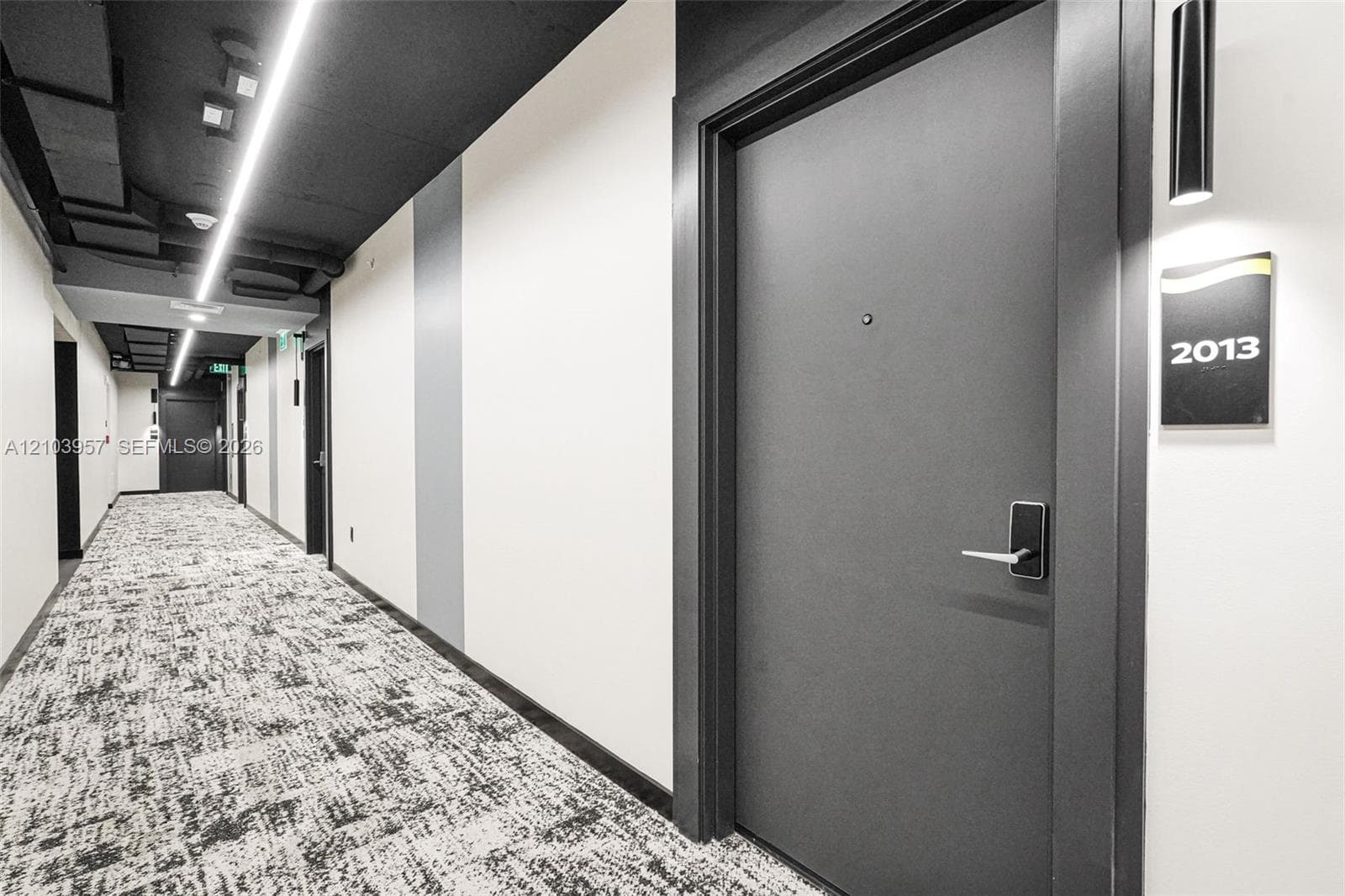 Modern hallway featuring patterned carpet flooring, white walls, and a dark ceiling with linear lighting fixtures