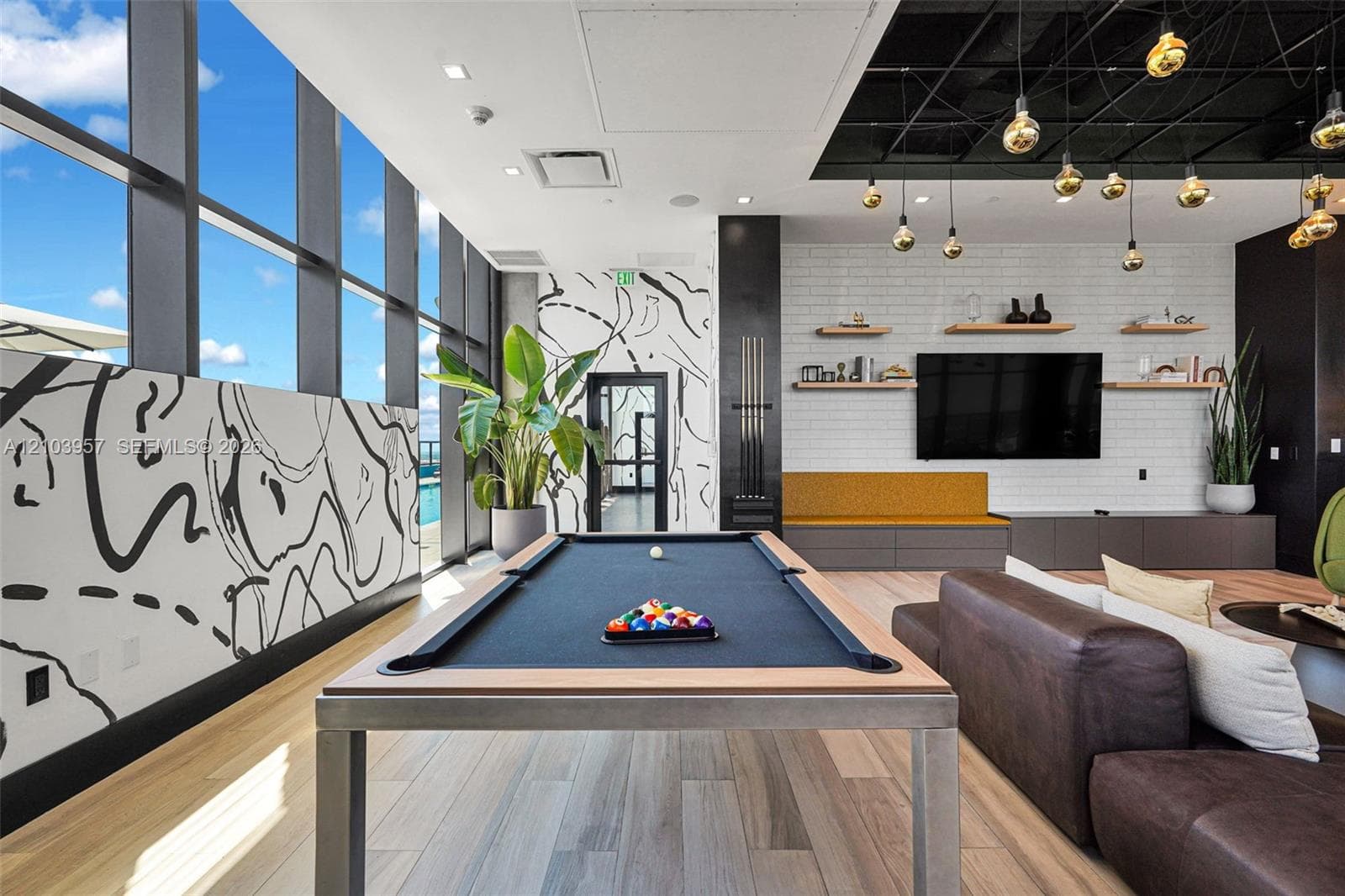 Floor-to-ceiling windows, wood-finish flooring, white brick accent wall, built-in shelving, and recessed lighting