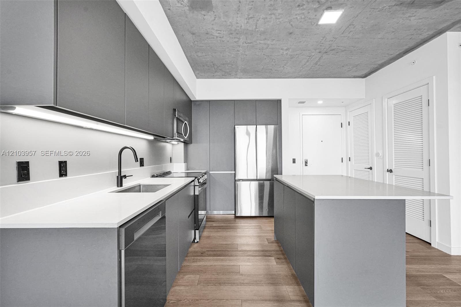Modern kitchen featuring light wood-finish flooring, white countertops, gray flat-panel cabinetry, stainless steel appliances, and a central island