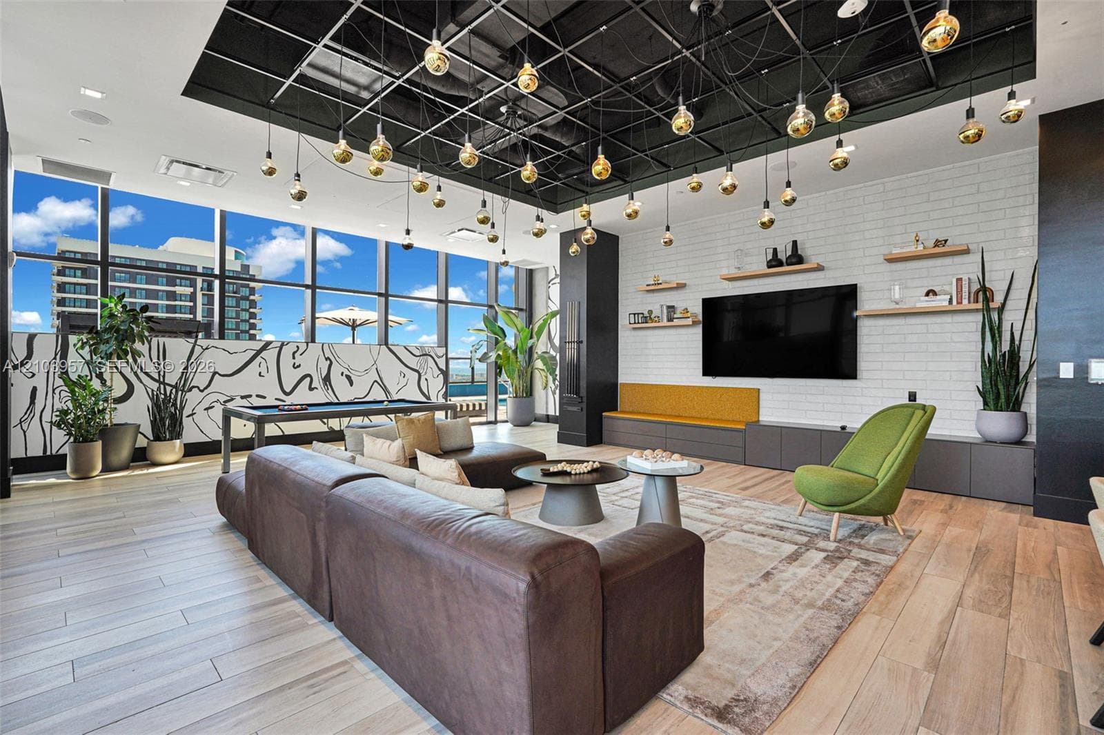 Expansive living area with large windows, wood-finish flooring, white brick-patterned accent wall, built-in shelving, and a unique grid-patterned ceiling with multiple pendant lights