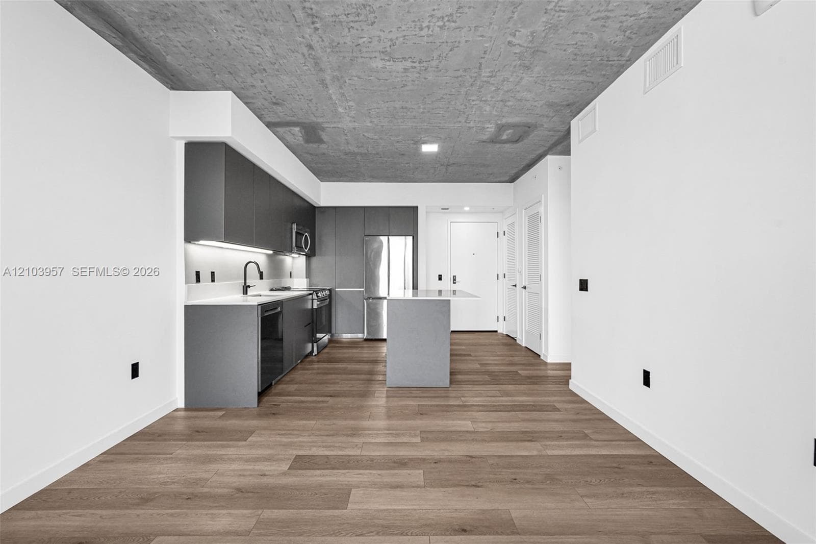 Modern kitchen featuring dark cabinetry, stainless steel appliances, light-toned countertops, a kitchen island, and wood-finish flooring