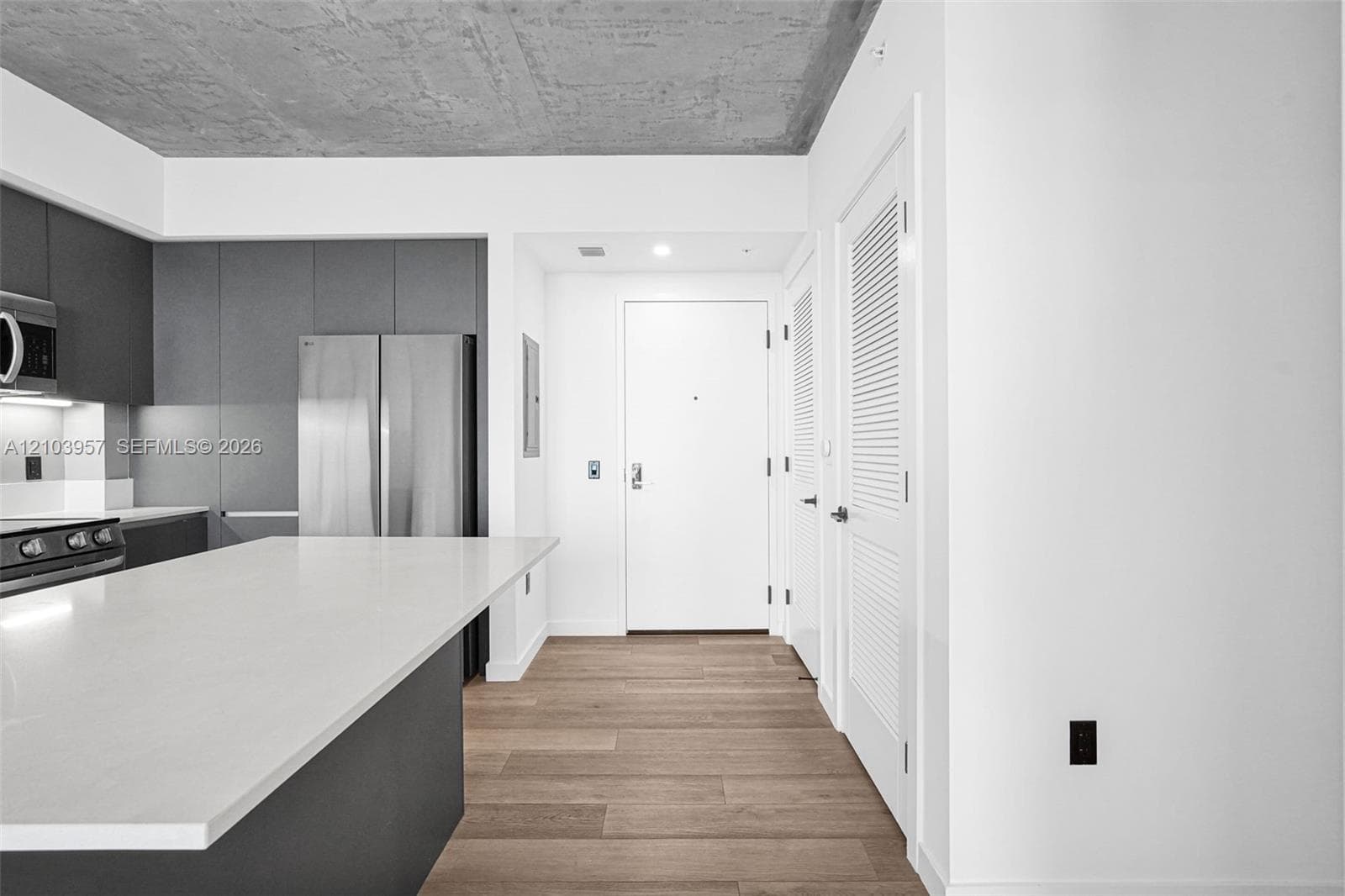 Kitchen featuring a large island with a white countertop, dark flat-panel cabinetry, stainless steel appliances, and a wood-finish floor