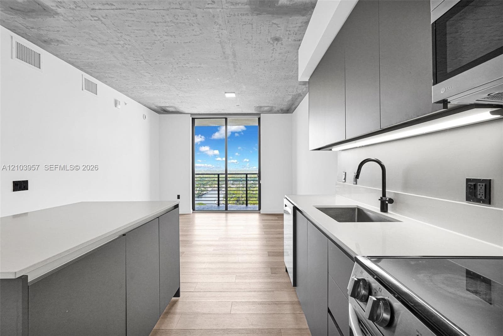 Kitchen featuring dark gray cabinetry, light wood-finish flooring, white countertops, and a stainless steel sink with a matte black faucet