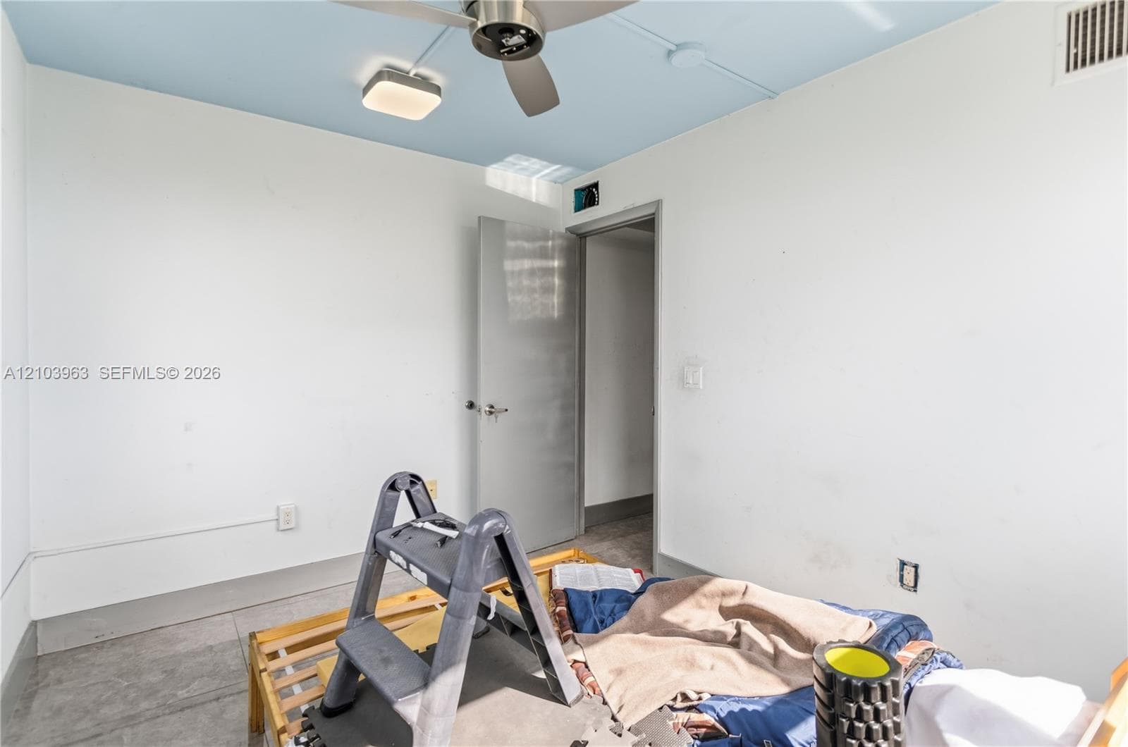 Neutral interior space featuring a light blue ceiling, gray tile flooring, a silver-toned ceiling fan with integrated lighting, and a single-panel interior door