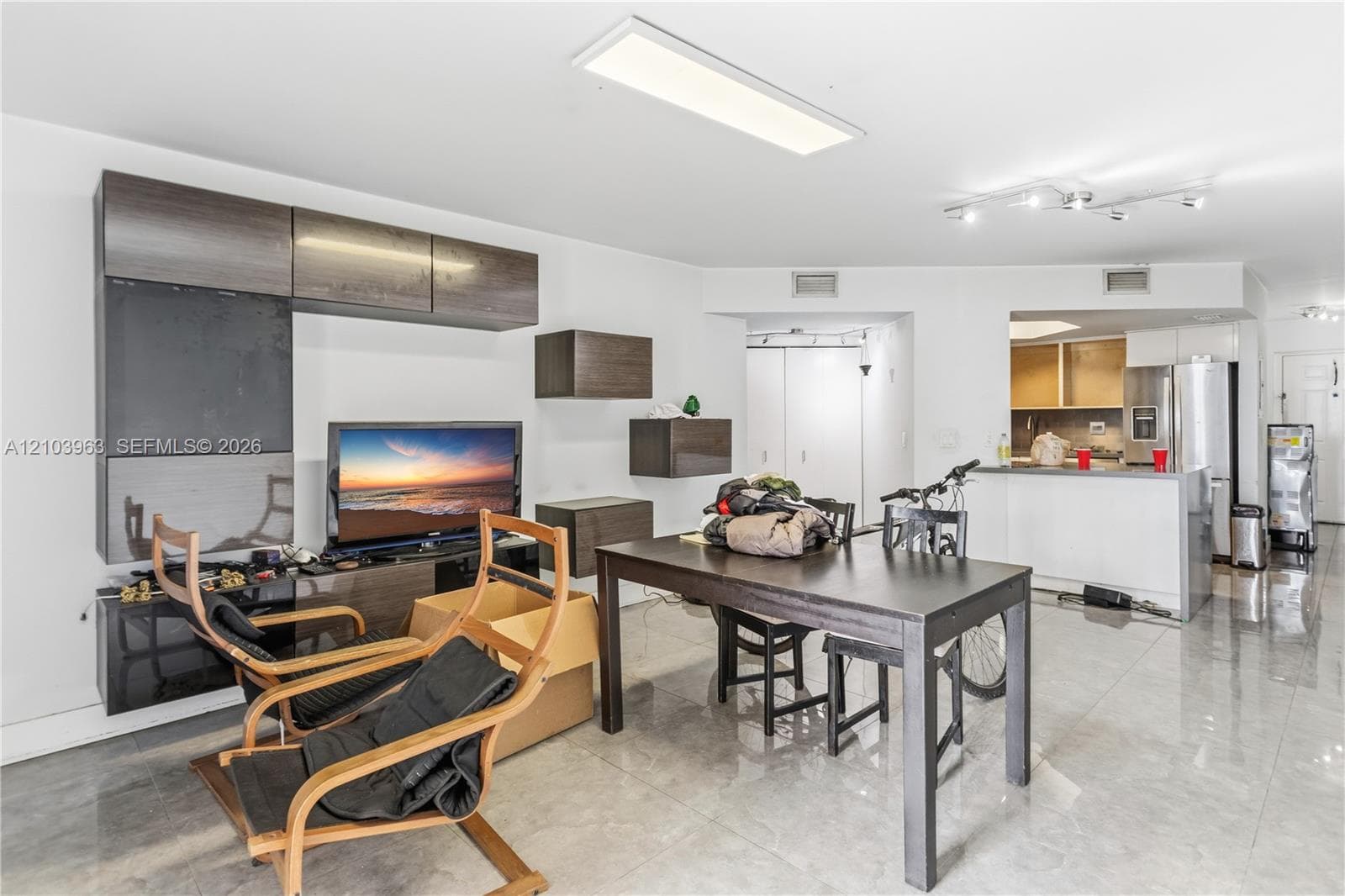 Open-concept living space featuring high-gloss tile flooring, dark wood-finish wall-mounted cabinetry, flush-mount LED lighting, and a breakfast bar
