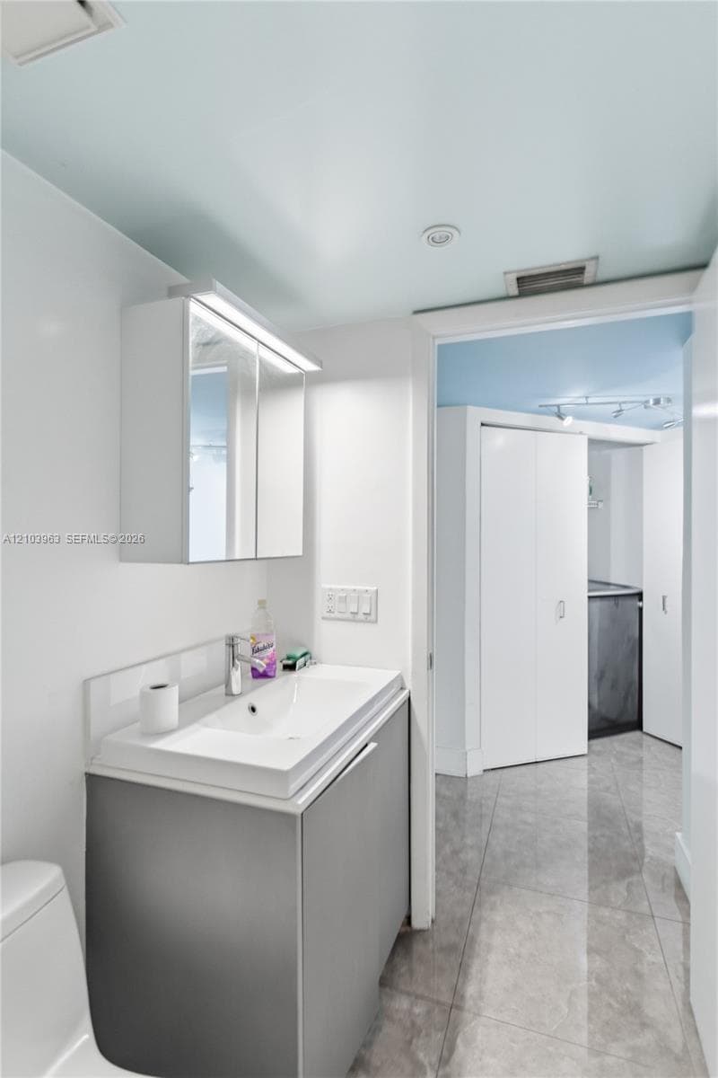 Modern vanity featuring a rectangular integrated sink, neutral cabinetry, and an illuminated mirrored medicine cabinet, complemented by large-format tile flooring