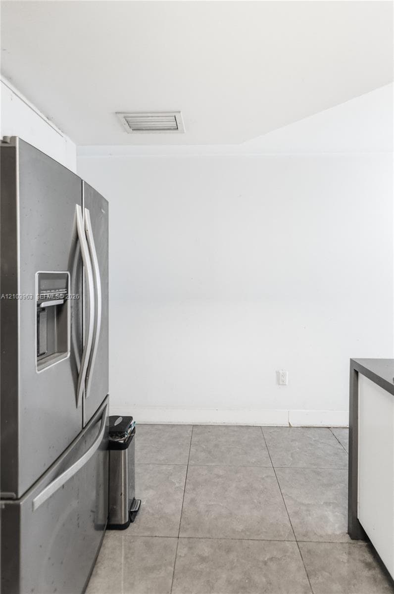Stainless steel French door refrigerator with an integrated water dispenser and large-format tile flooring