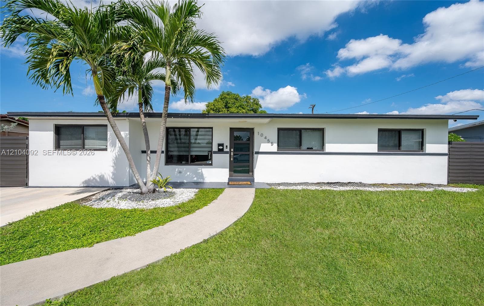 Mid-century modern exterior featuring white stucco finish, dark-trimmed horizontal detailing, dark metal-framed windows, a glass-panel entry door, and a concrete walkway