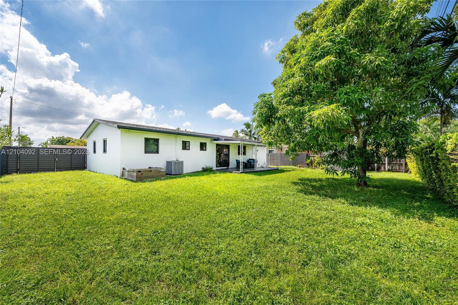 Expansive backyard featuring a sprawling lawn, mature trees, concrete patio, and full perimeter fencing