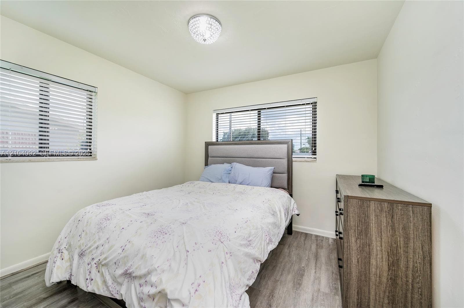 Room featuring wood-finish flooring, dual windows with horizontal blinds, and a circular flush-mount crystal light fixture