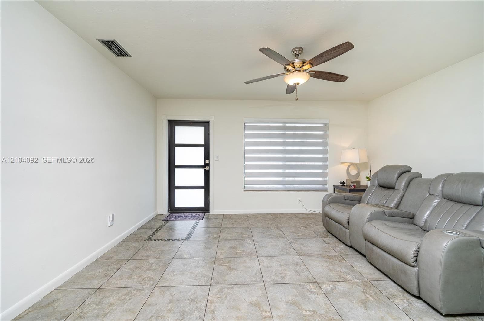 Neutral-toned tile flooring, four-panel glass-inset entry door, ceiling fan with integrated lighting, and horizontal window blinds