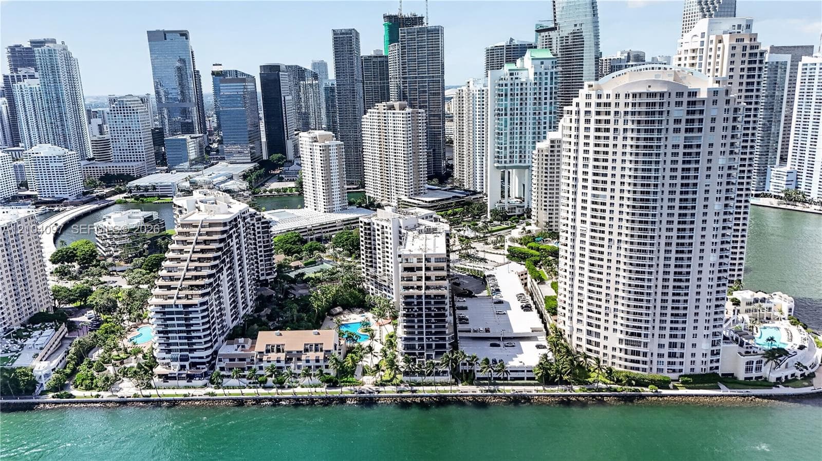 Aerial perspective of a waterfront high-rise urban district featuring multi-story residential structures, coastal seawalls, swimming pools, and extensive palm-lined landscaping