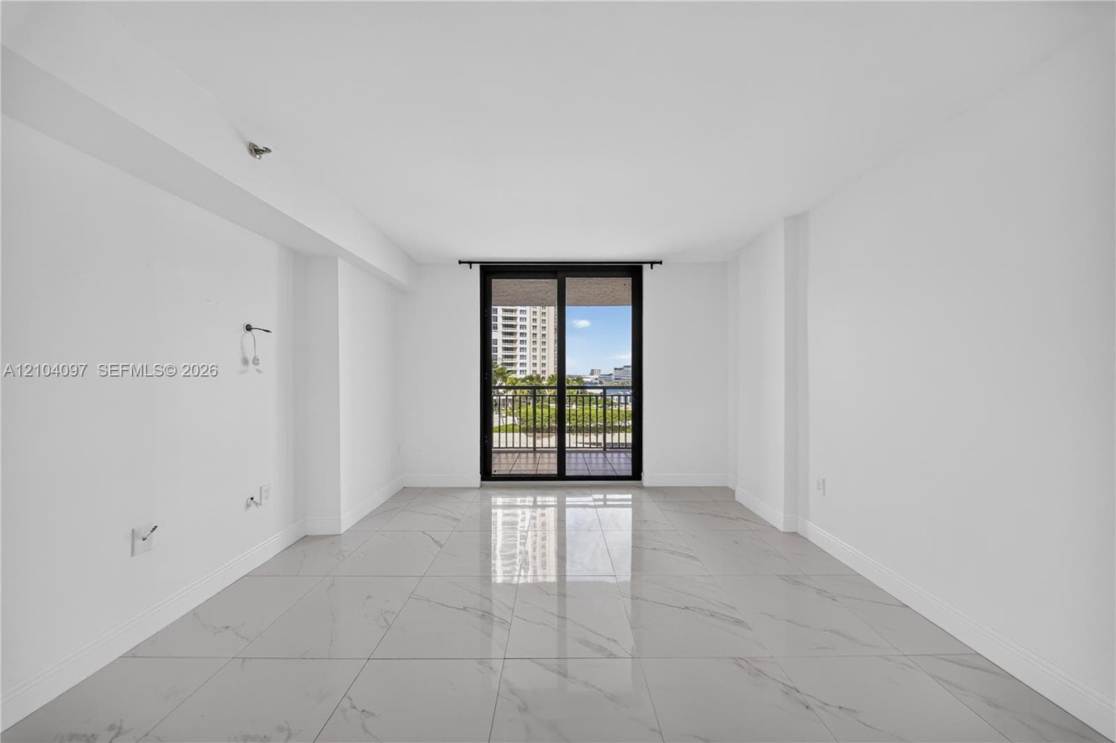 Interior room featuring polished large-format stone-style flooring, white walls, and a sliding glass door with a dark metal frame